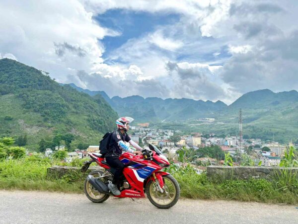 Motorbike rider on a high mountain road overlooking Meo Vac town nestled in the valley below