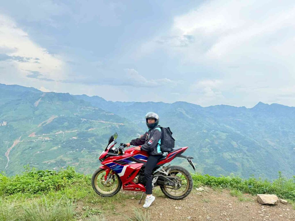 Motorbike rider on a high mountain pass looking down at the winding Nho Que River far below