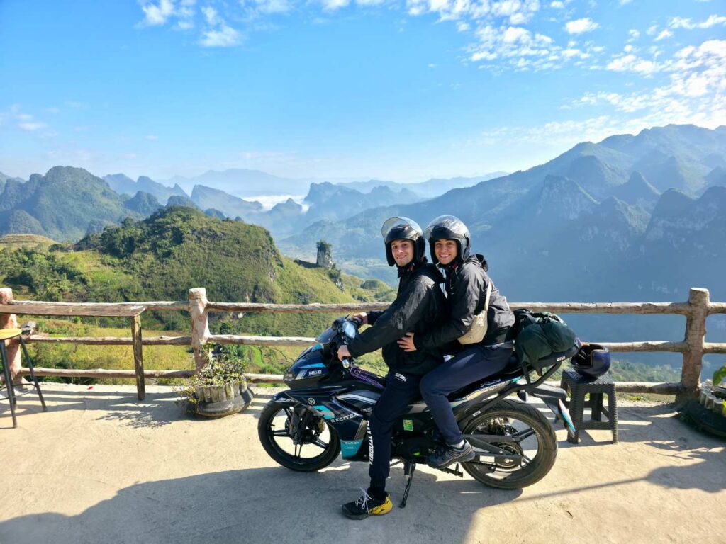 Motorbike riders on winding mountain road in Ha Giang Loop with steep cliffs and dense green hills in background